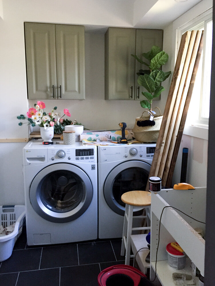 unfinished laundry room makeover with white walls, wood against the window and unbuilt cabinet