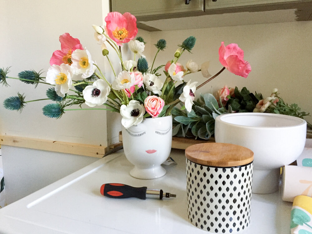polka dot canister, celfie vase and faux flowers sitting on top os washing machine