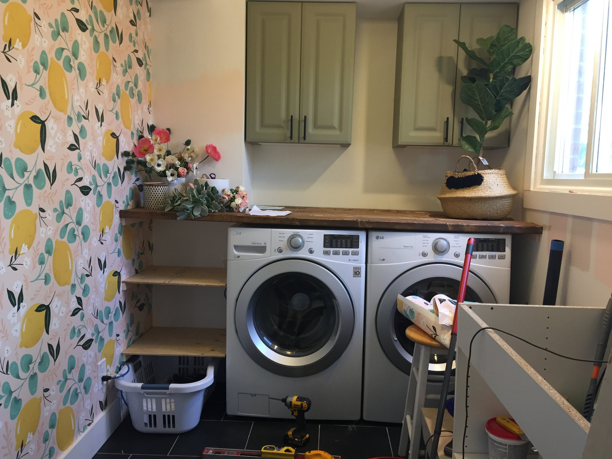 laundry room with lemon wallpaper and green cabinets, messy with tools and flowers
