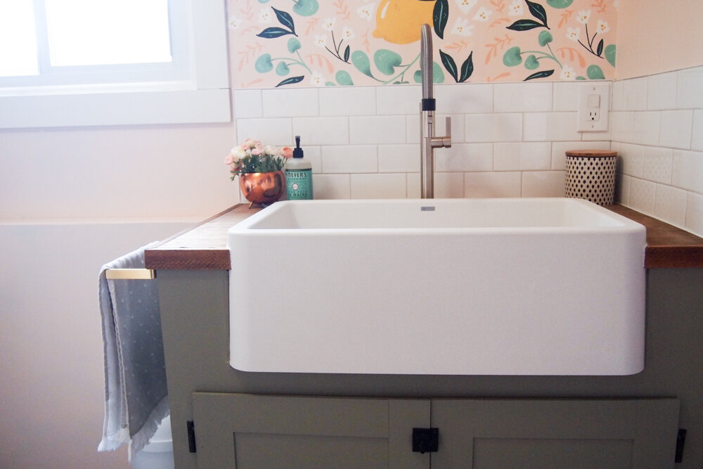 apron front sink with wood countertop and green cabinets, white subway tile, pink walls and lemon wallpaper