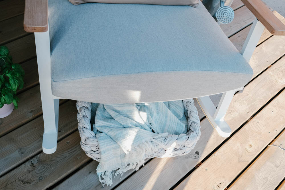 View from above of modern white and grey rocking chair, white washed basket with light blue blanket inside.