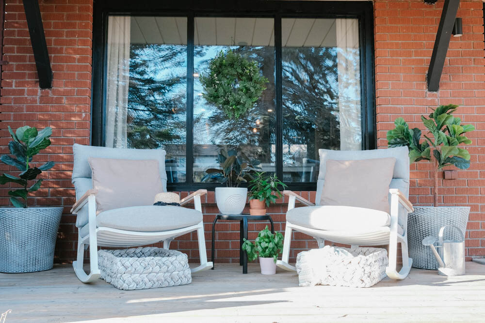 Front porch with red brick, black window trim, modern Eleya white and grey rocking chairs from Article, Tress white washed trays under chairs and two large white washed pots on either side with fiddle leaf fig trees.