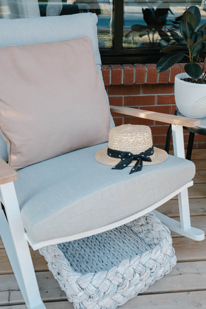 Eleya cera grey and white rocking chair from Article with Tress white washed tray, and cushion Belez in Yuma Mink Taupe. Straw hat with navy blue ribbon sitting on the rocking chair.
