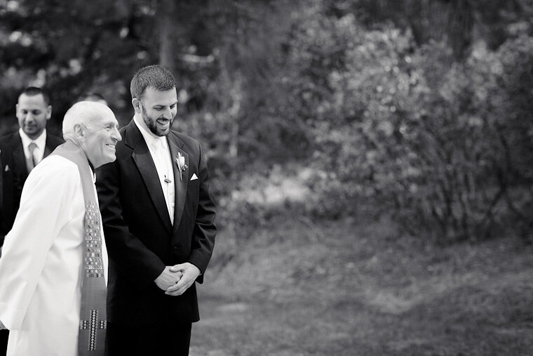 Groom and priest laugh together before wedding starts.