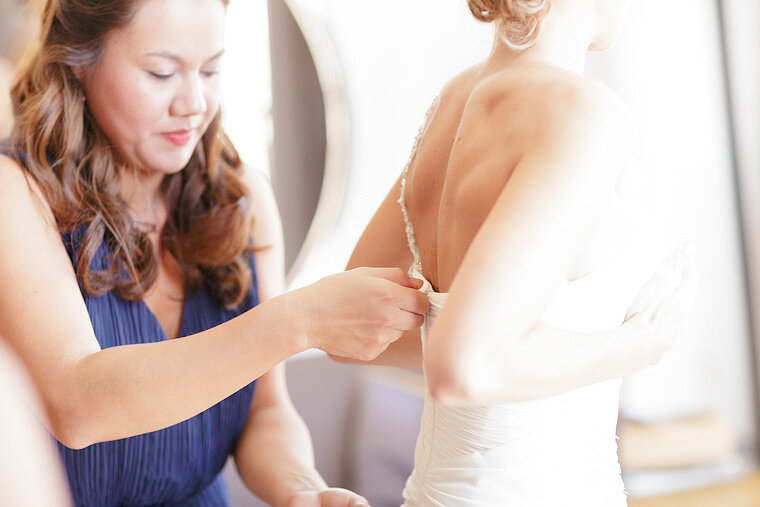 Maid of honor zips up bride's dress.