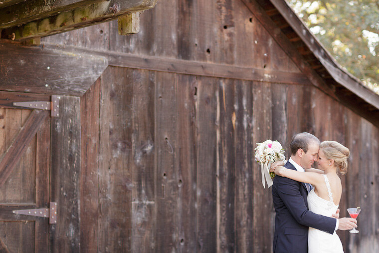 Bride and groom kiss near old barn.