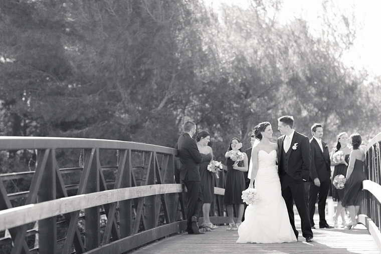 Bride and groom stop for a kiss on the bridge with bridal party behind them.