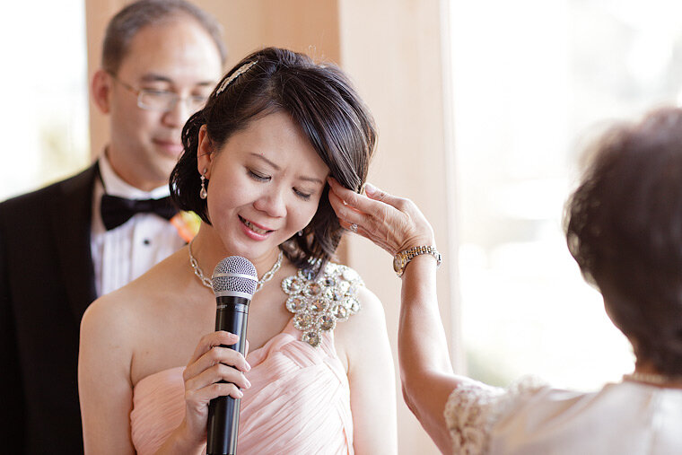Groom looks on while bride gives teary speech at a wedding reception.