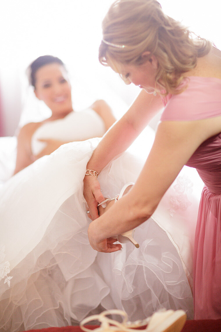 Maid of honor puts bride's shoes on.