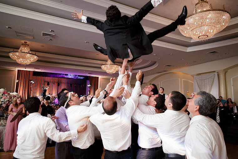 The groom is tossed in the air by the groomsmen.