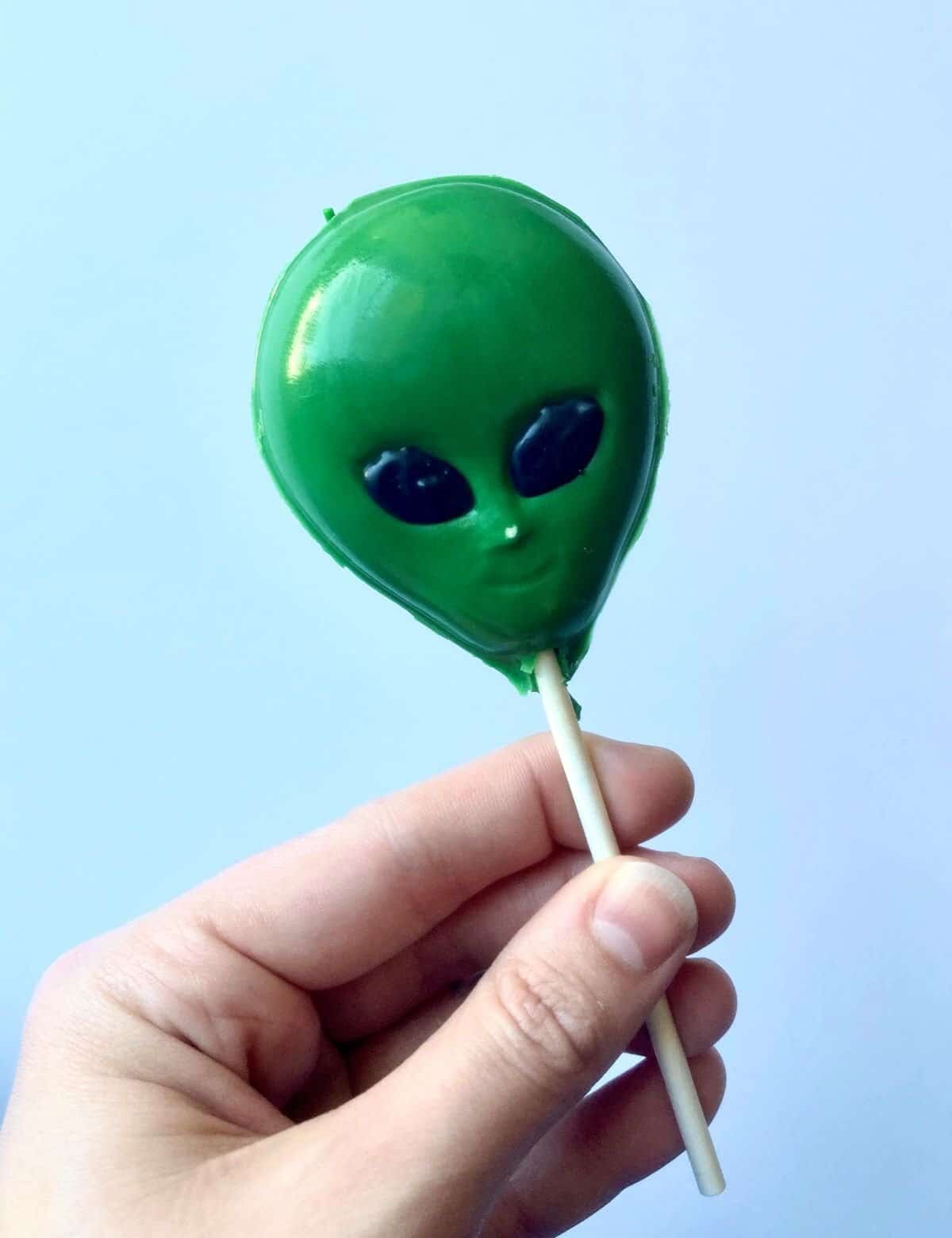 hand holding cake pop in the shape of an alien head