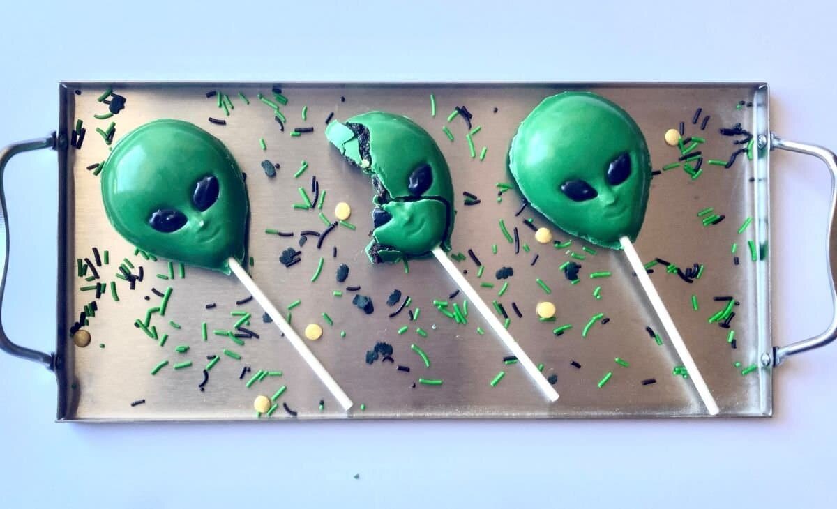 Tray of three alien cake pops with a bite taken out of the middle cake pop.