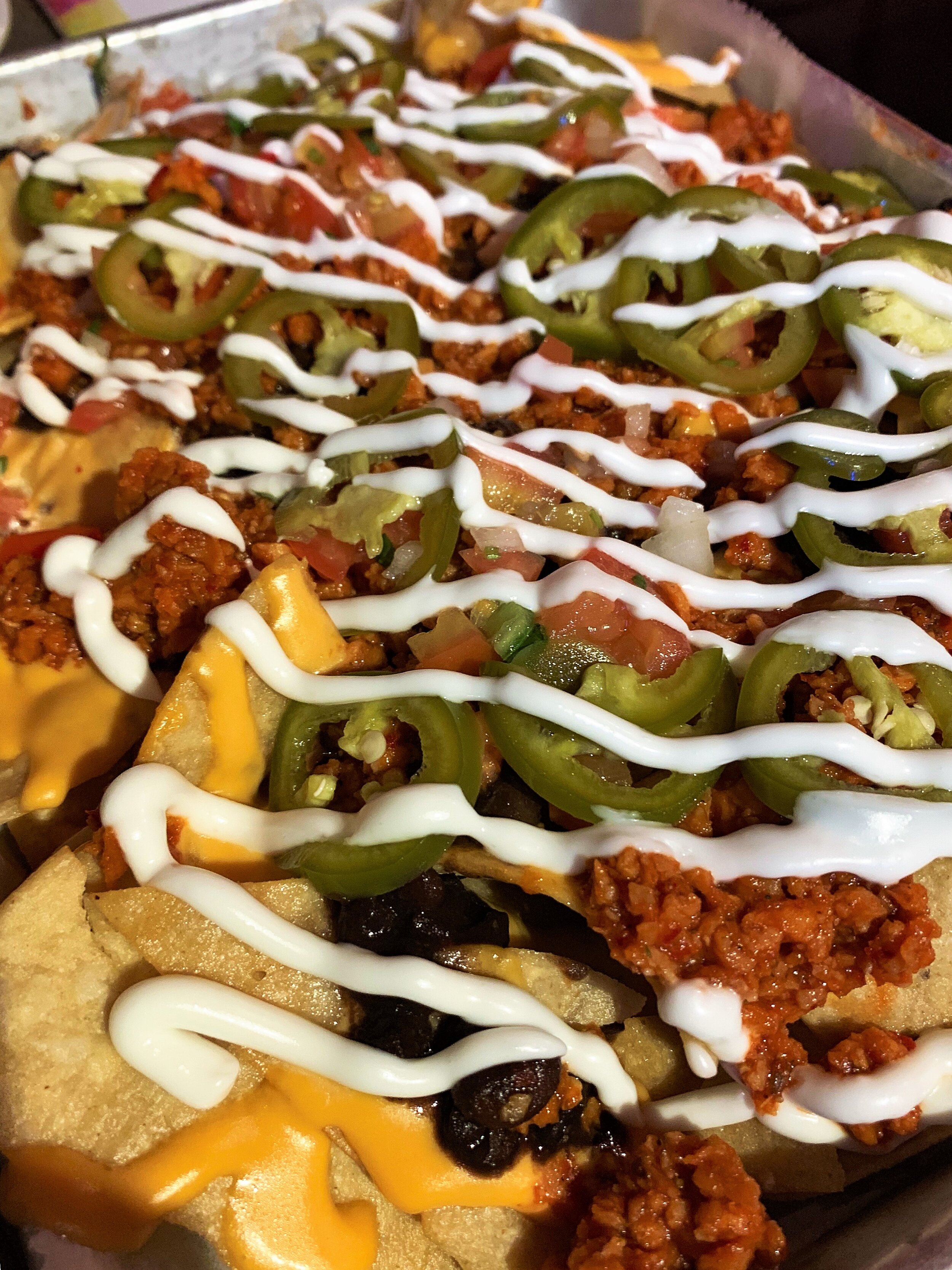 Nacho chips topped with vegan cheese and sour cream, soy chorizo, black beans, and jalapeños.