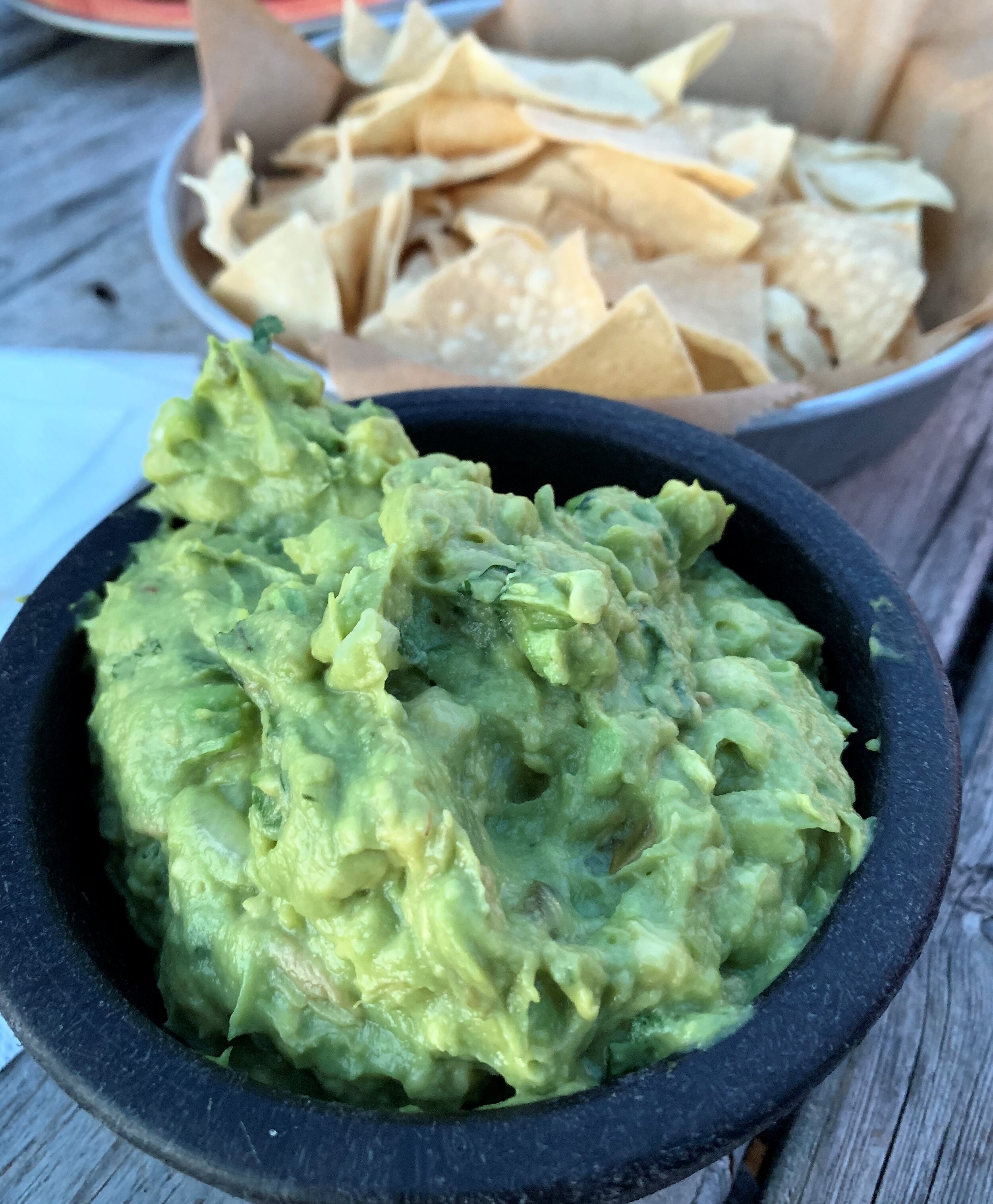 a dish of guacamole with tortilla chips in the background