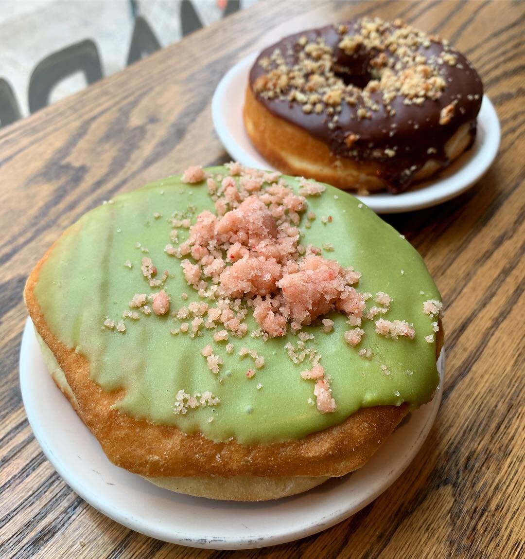 A donut with green matcha frosting and pink sugar sprinkled on top, and another donut in the background with chocolate frosting and chopped hazelnuts on top at Dottie's Donuts in Philadelphia