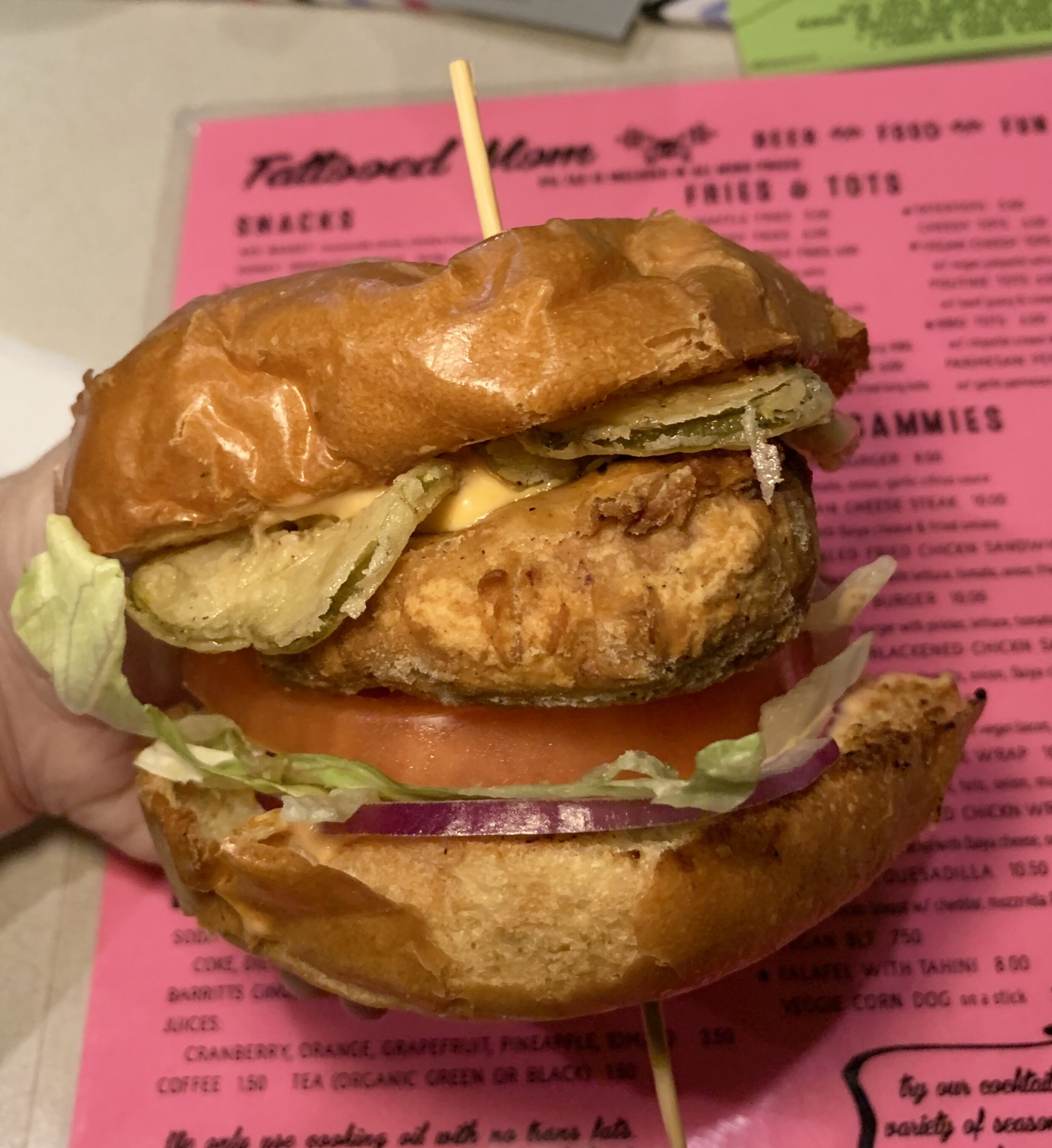 a vegan fried chicken sandwich with onion, lettuce, tomato, fried pickles, and mayo