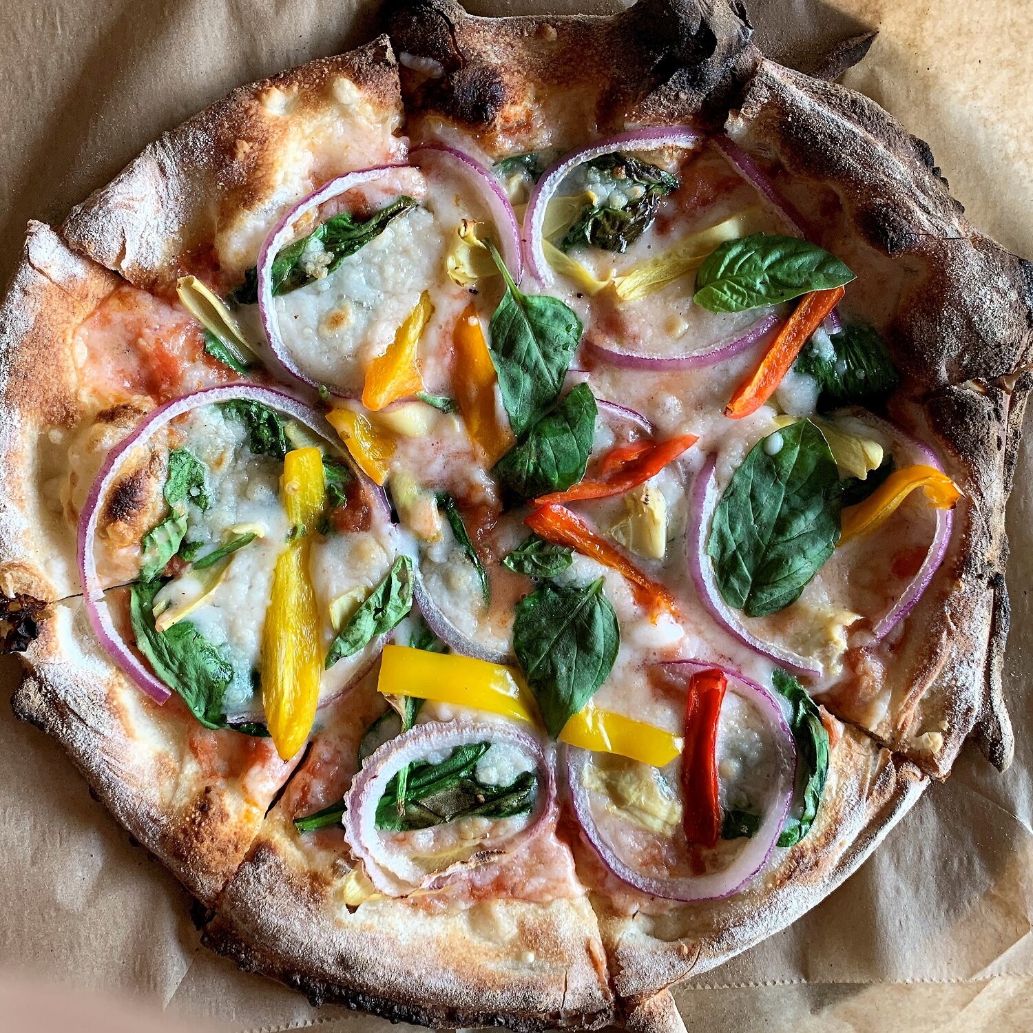 A thin crust pizza with vegan cheese, peppers, spinach, and red onions