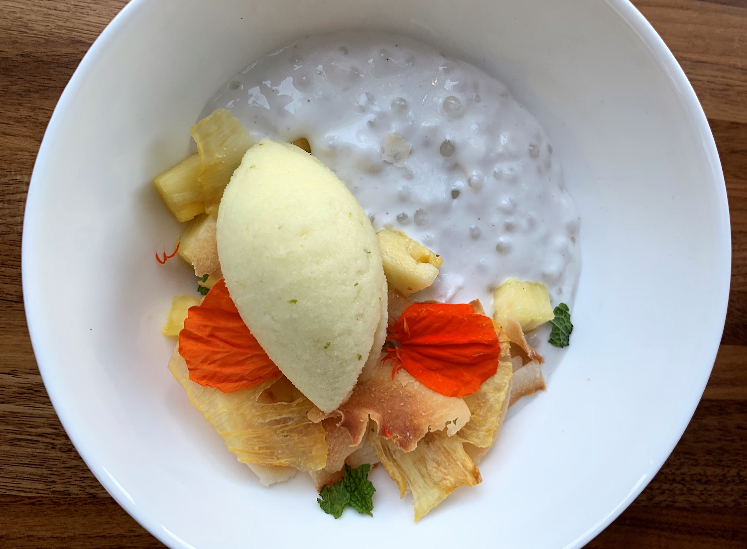 a bowl of tapioca pudding topped with pineapple sorbet, toasted coconut flakes, and flower petals