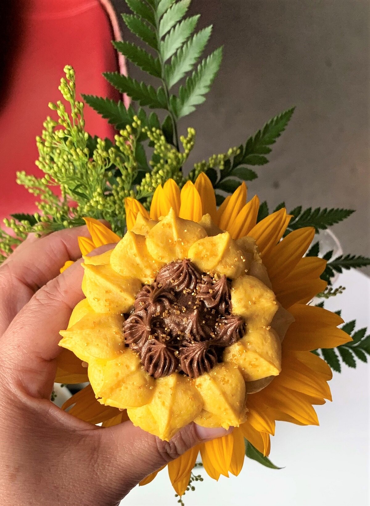 sunflower icing on a cupcake with a sunflower behind it