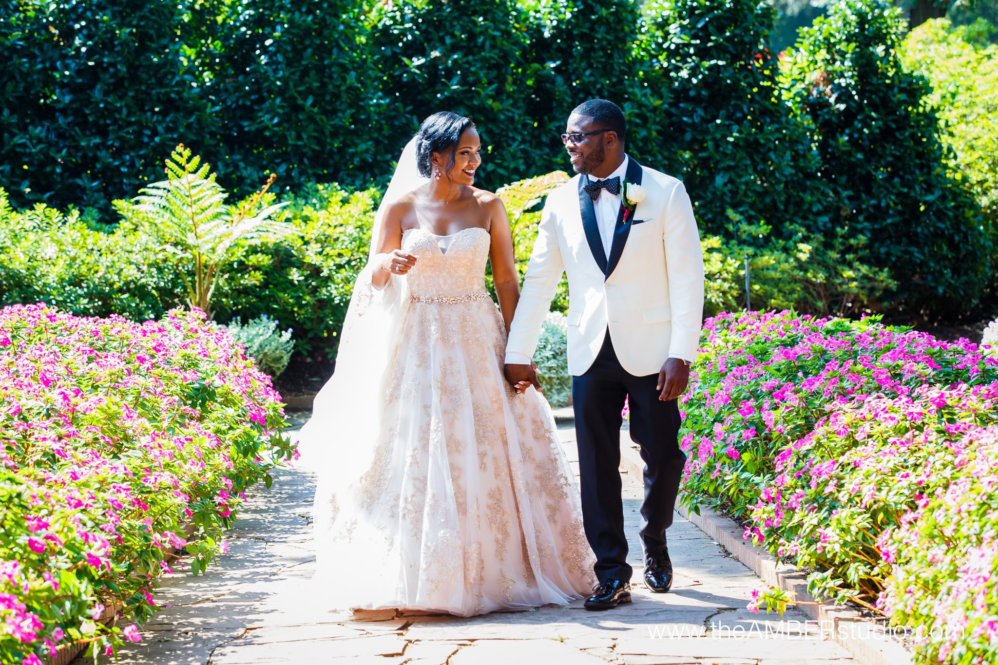 African American bride & groom at the Dallas Arboretum & Botanical Garden. It is sunny, and they are holding hands and walking in the garden on their wedding day.