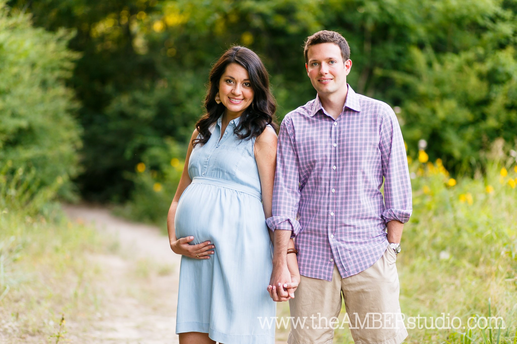 Multicultural couple holding hands at their maternity session in the fields at White Rock Lake with Texas wildflowers behind them.