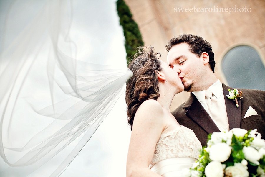 bride and groom kissing with veil blowing in wind