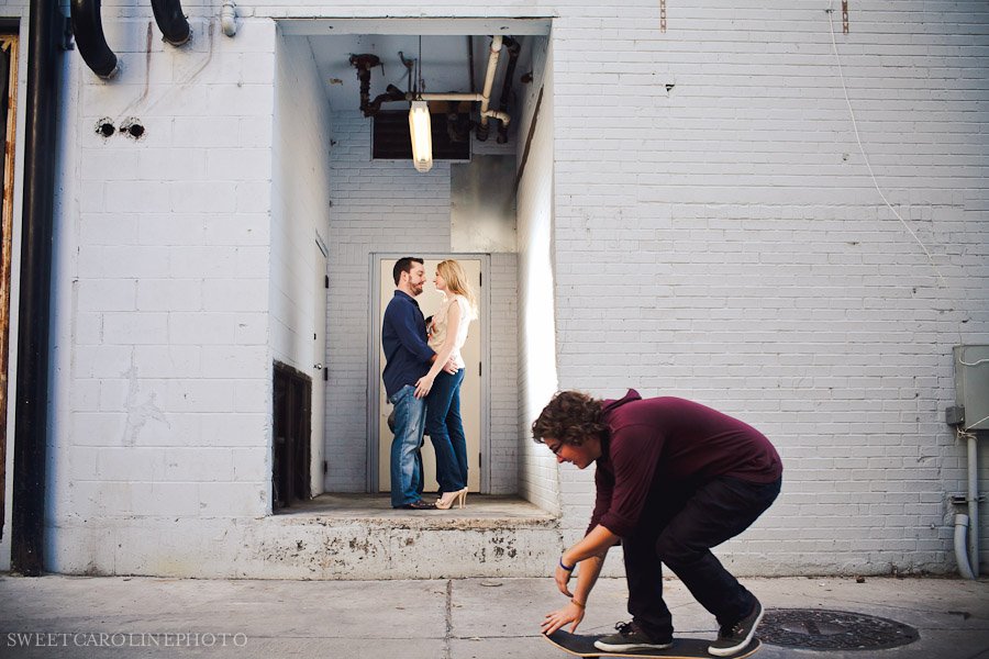 couple in alley way with skateboarder rolling by