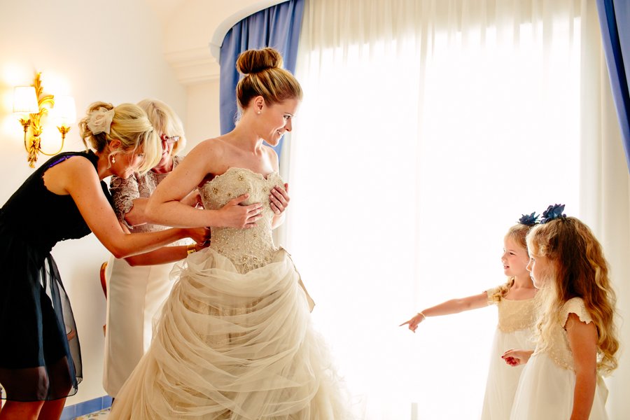 bride putting on dress with flower girls