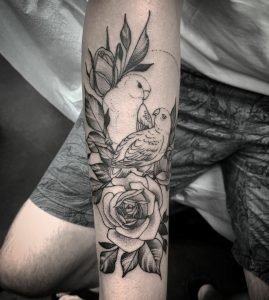 Two birds with roses blackwork tattoo by Jesse Iris on a client's arm.