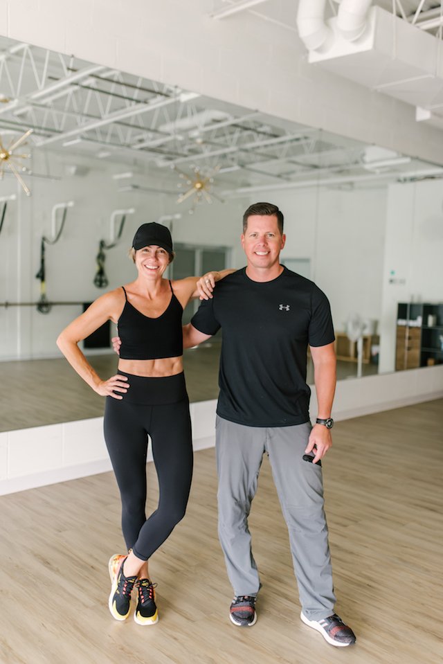 seersucker + mark morgan fitness by popular Indianapolis fitness blog, Seersucker and Saddles: image of a woman standing next to a man and resting her elbow on his shoulder inside a workout room.
