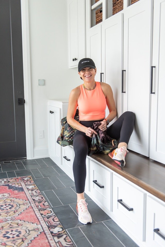 Gym Bag Essentials by popular Indianapolis life and style blog, Seersucker and Saddles: image of a woman wearing Nike Air Max 270, Lululemon Baller Hat, and Athleta Conscious Crop in Powervita™ D-DD and sitting in front of a MZ Wallace Travel Jimmy.