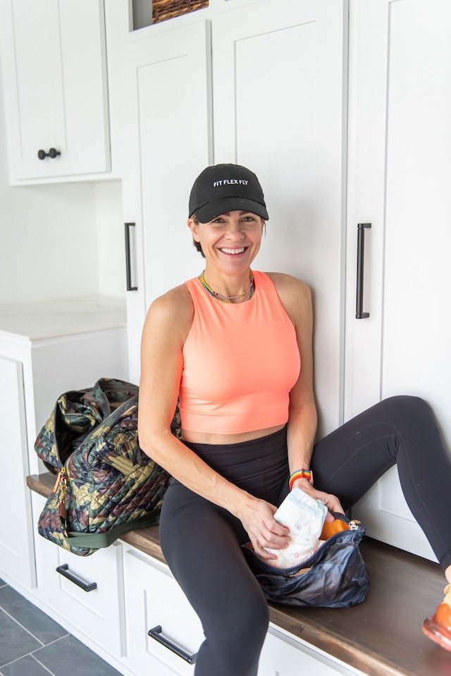 Gym Bag Essentials by popular Indianapolis life and style blog, Seersucker and Saddles: image of a woman wearing Nike Air Max 270, Lululemon Baller Hat, and Athleta Conscious Crop in Powervita™ D-DD and sitting in front of a MZ Wallace Travel Jimmy.