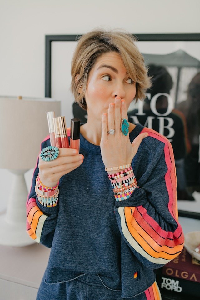 Clean Beauty Movement by popular Indianapolis beauty blog, Seersucker and Saddles: image of a woman holding four lipglosses in her hand and covering her mouth with her other hand. 