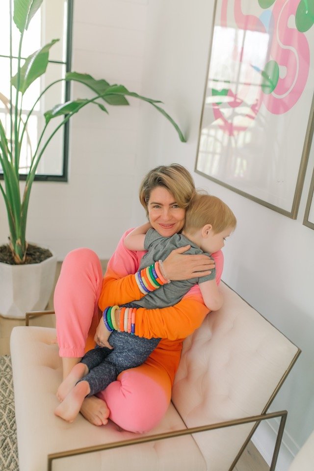 Espacio Stackers by popular Indianapolis fashion blog, Seersucker and Saddles: image of a woman sitting on a couch while holding her son and wearing Espacio fiesta stackers. 