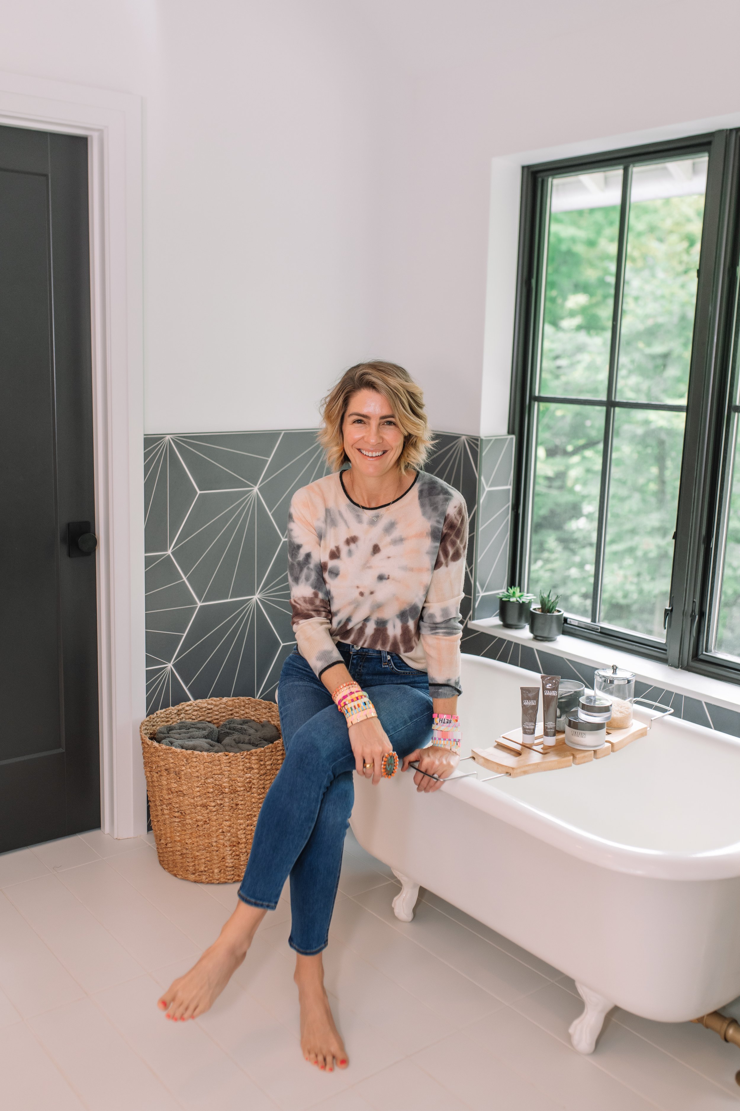 Colleen Rothschild by popular Indianapolis beauty blog, Seersucker and Saddles: image of a woman sitting on the edge of her claw foot tub next to a tub tray containing various Colleen Rothschild products. 