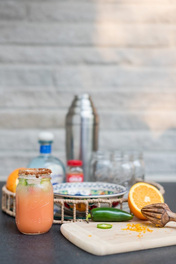The Love of the Bowl by popular Indianapolis lifestyle blog, Seersucker and Saddles: image of spicy Paloma drink in a mason jar next to a cutting board with a jalapeno and cut orange on it. 