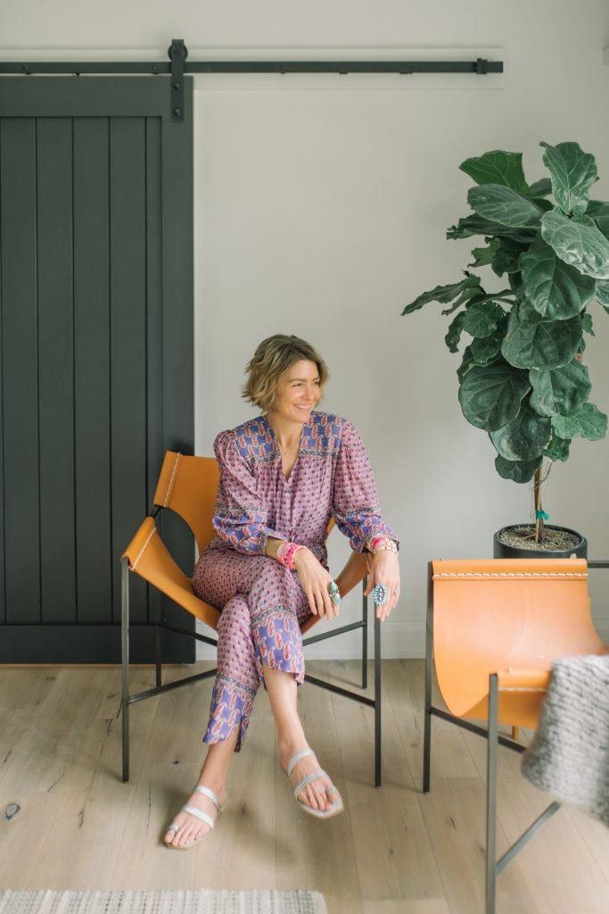 Global Healing by popular Indianapolis lifestyle blog, Seersucker and Saddles: image of a woman wearing a floral and paisley jumpsuit and sitting in a leather chair. 