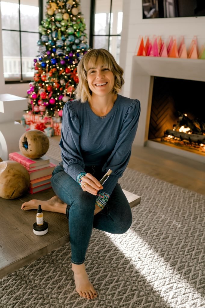 Self Care with Equilibria by popular Indianapolis lifestyle blog, Seersucker and Saddles: image of Beth Chappo sitting in her living room and holding Equilibria products in her hands. 