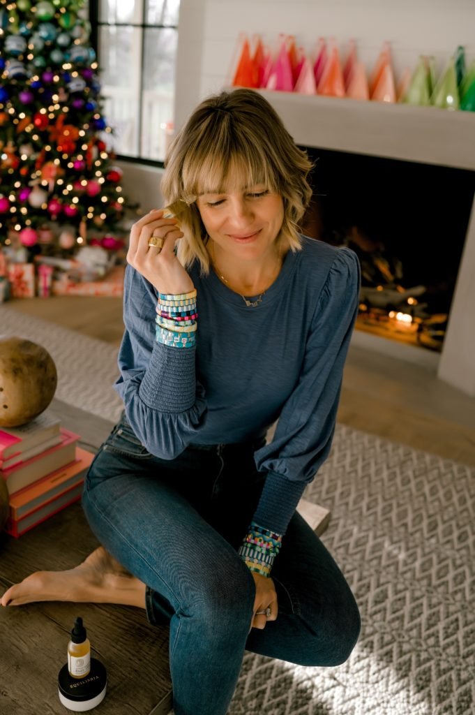 Self Care with Equilibria by popular Indianapolis lifestyle blog, Seersucker and Saddles: image of Beth Chappo sitting in her living room and holding Equilibria products in her hands. 