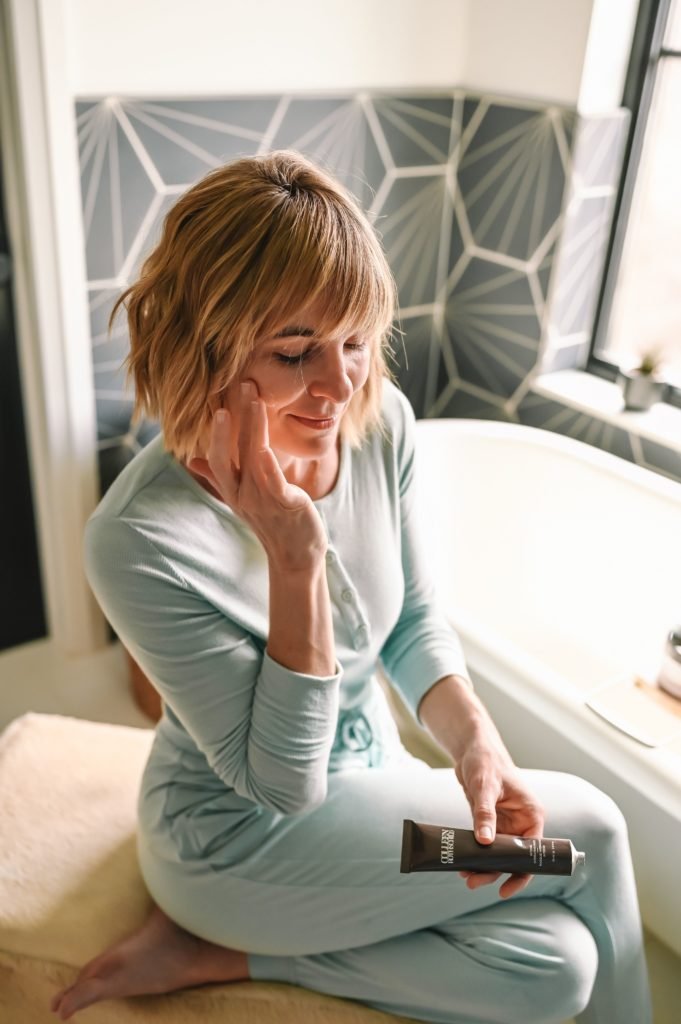 Colleen Rothschild BOGO by popular Indianapolis beauty blog, Seersucker and Saddles: image of a woman wearing a light blue loungewear set and sitting next to her tub while holding some Colleen Rothschild products. 