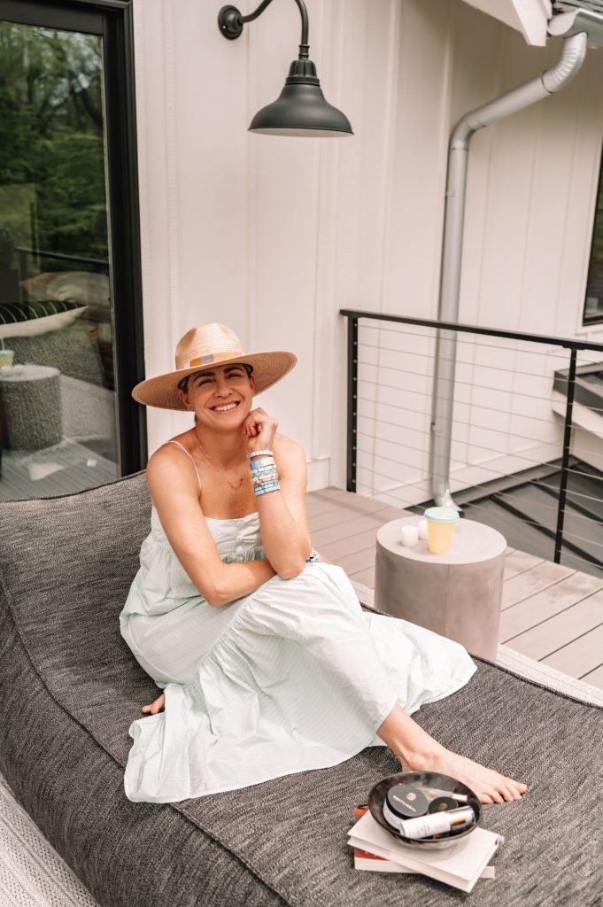 Equilibria Memorial Day Sale by popular Indianapolis lifestyle blog, Seersucker and Saddles: image of a woman wearing a straw fedora and light blue ruffle hem maxi dress while sitting outside next to some Equilibria products. 
