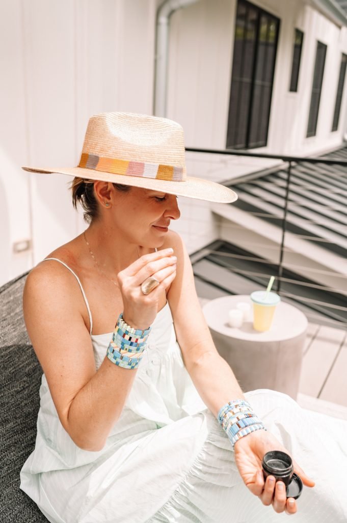 Equilibria Memorial Day Sale by popular Indianapolis lifestyle blog, Seersucker and Saddles: image of a woman wearing a straw fedora and light blue ruffle hem maxi dress while holding a Equilibria product. 