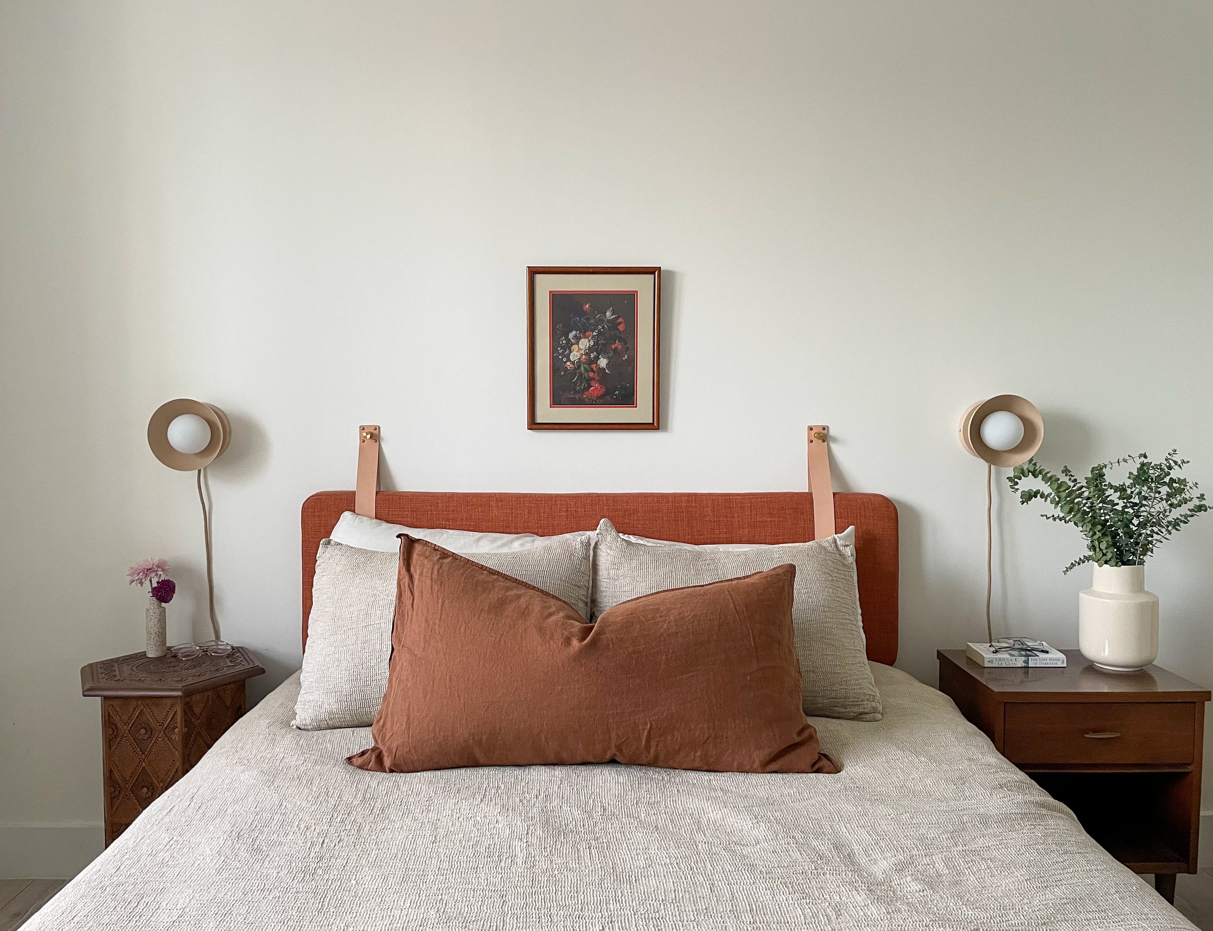 A head-on shot of a bed. There is a wall-hung headboard and a large brown throw pillow on it.