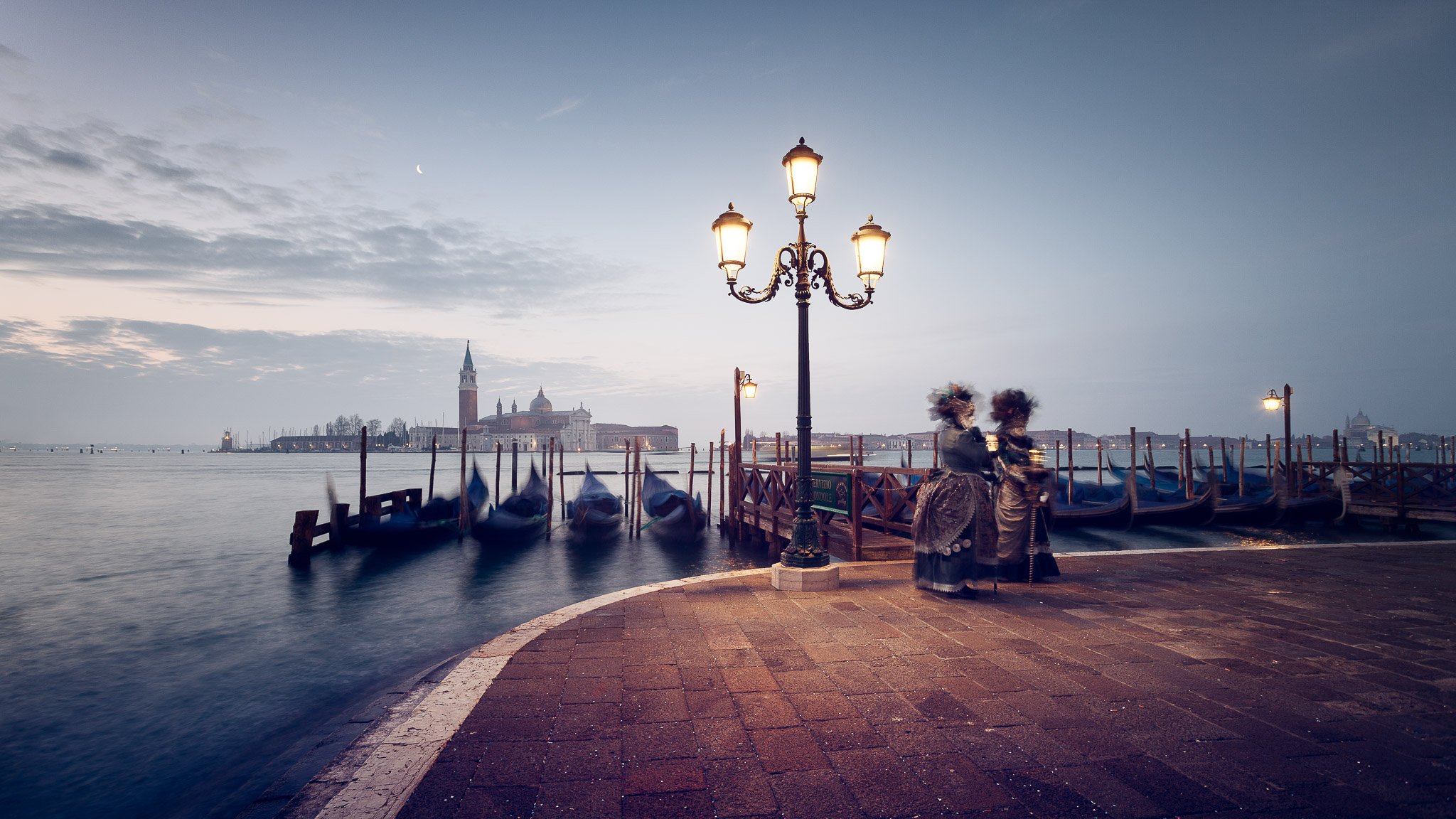 A couple of masked and costumed carnival attendants pose for photographers at sunrise in venice