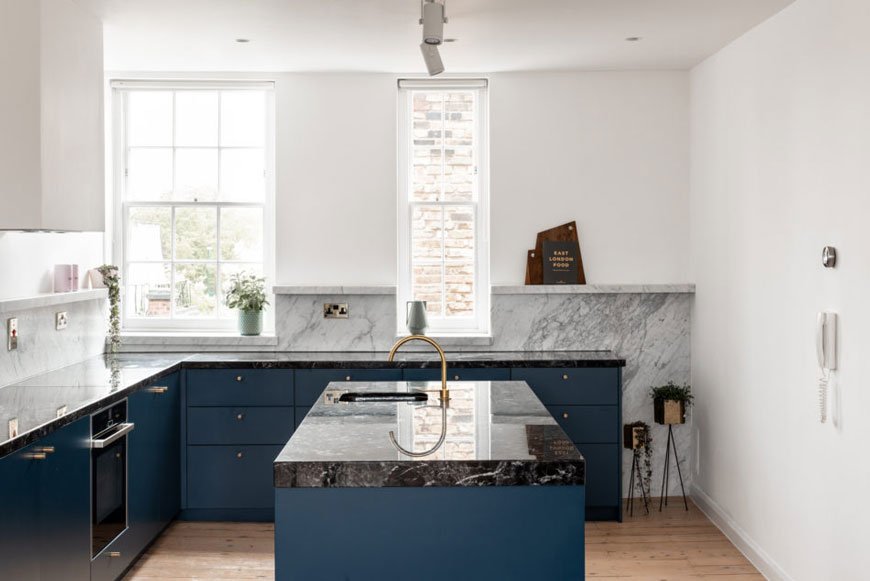 A blue kitchen with grey marble backsplash in a Hackney home in London.