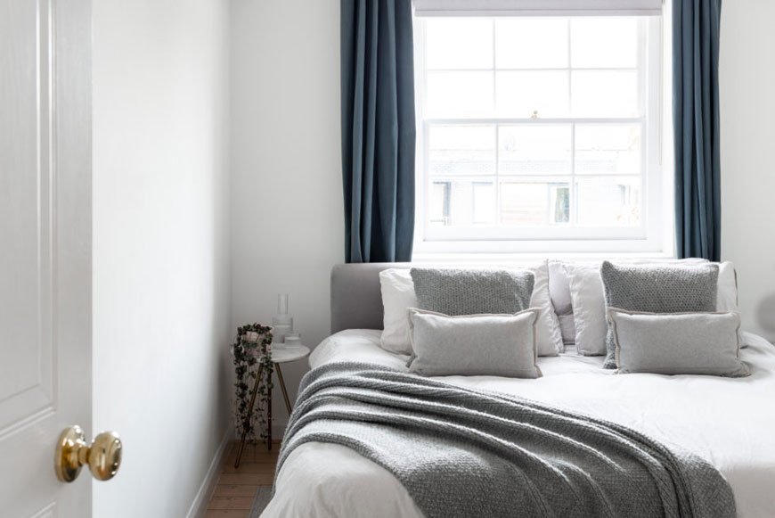 A Scandinavian styled bedroom with grey and white bedding and blue curtains in a Hackney home.