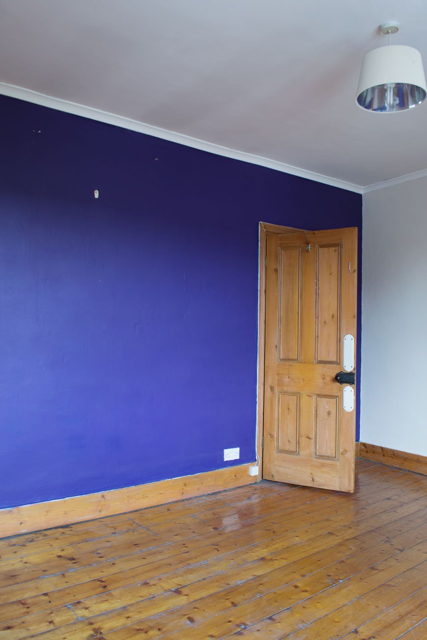 A deep purple feature wall and orange pine floorboards before our Nordic luxe bedroom makeover