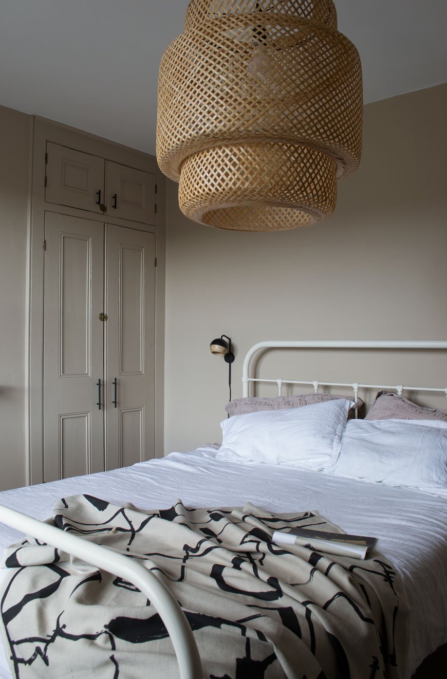 A white metal hospital style bed inside a beige bedroom with a bamboo lamp shade with Nordic luxe style. 
