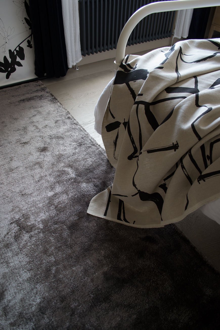 Looking onto a grey rug and an abstract art style bed throw inside a Nordic luxe style bedroom.