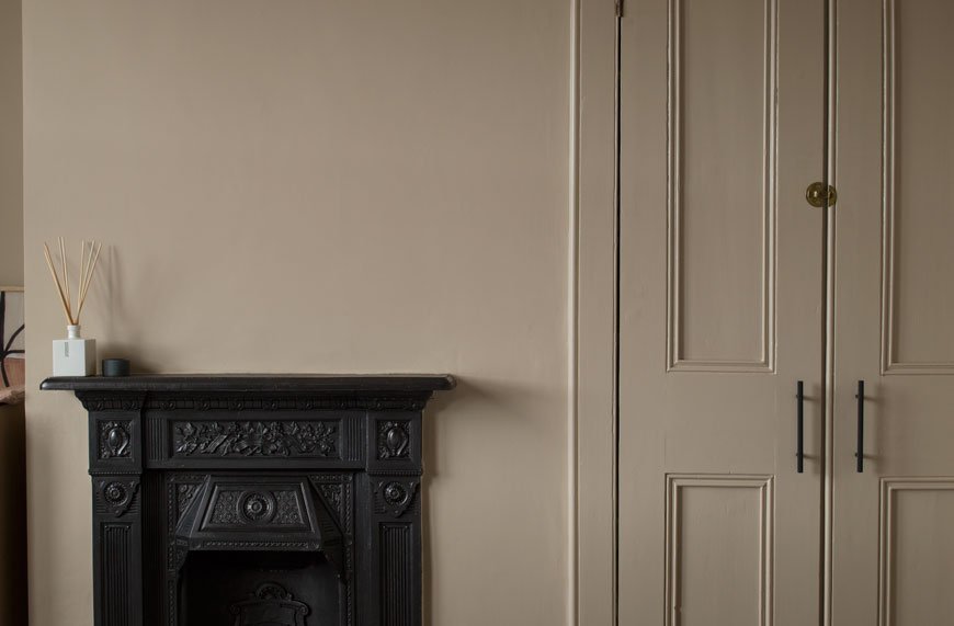 A wrought iron fireplace and Victorian cupboard doors in a beige Nordic luxe bedroom.